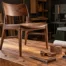 A finely crafted wooden chair on a workshop bench beside precision tools, joinery samples, and a furniture drawing.